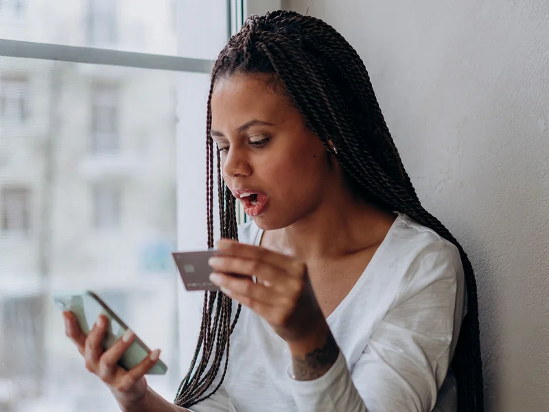 A woman using her smartphone with a payment card in hand.