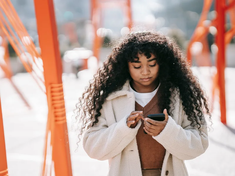 A woman using her smartphone on a bright city walkway.